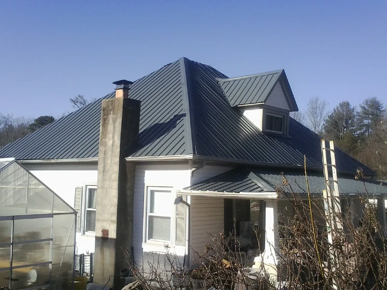 Dark blue standing seam metal roof on a white farmhouse with dormer — Slate & Tile Roof Repair by Roofing Brothers in Kintnersville