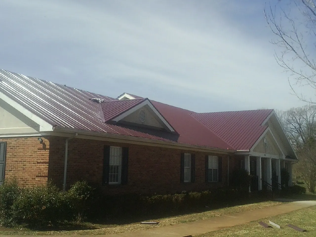 Red metal roof with gabled entries on a long brick building, from a Hail Damage Roof Repair job in Kintnersville