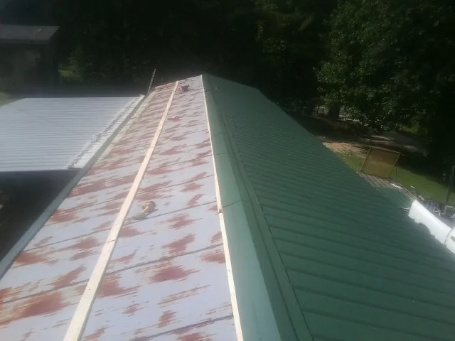 Old rusted panels beside newly installed green metal roofing — Wind Damage Roof Repair by Roofing Brothers in Kintnersville