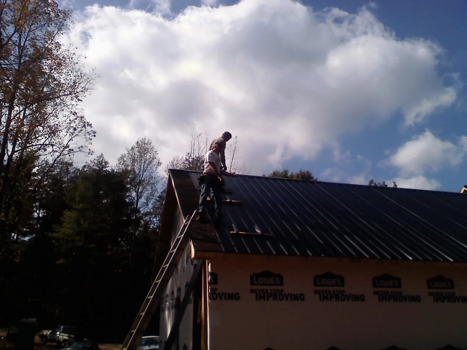 Roofer fastening dark metal panels high against a cloudy sky, from a Roof Inspection job in Kintnersville