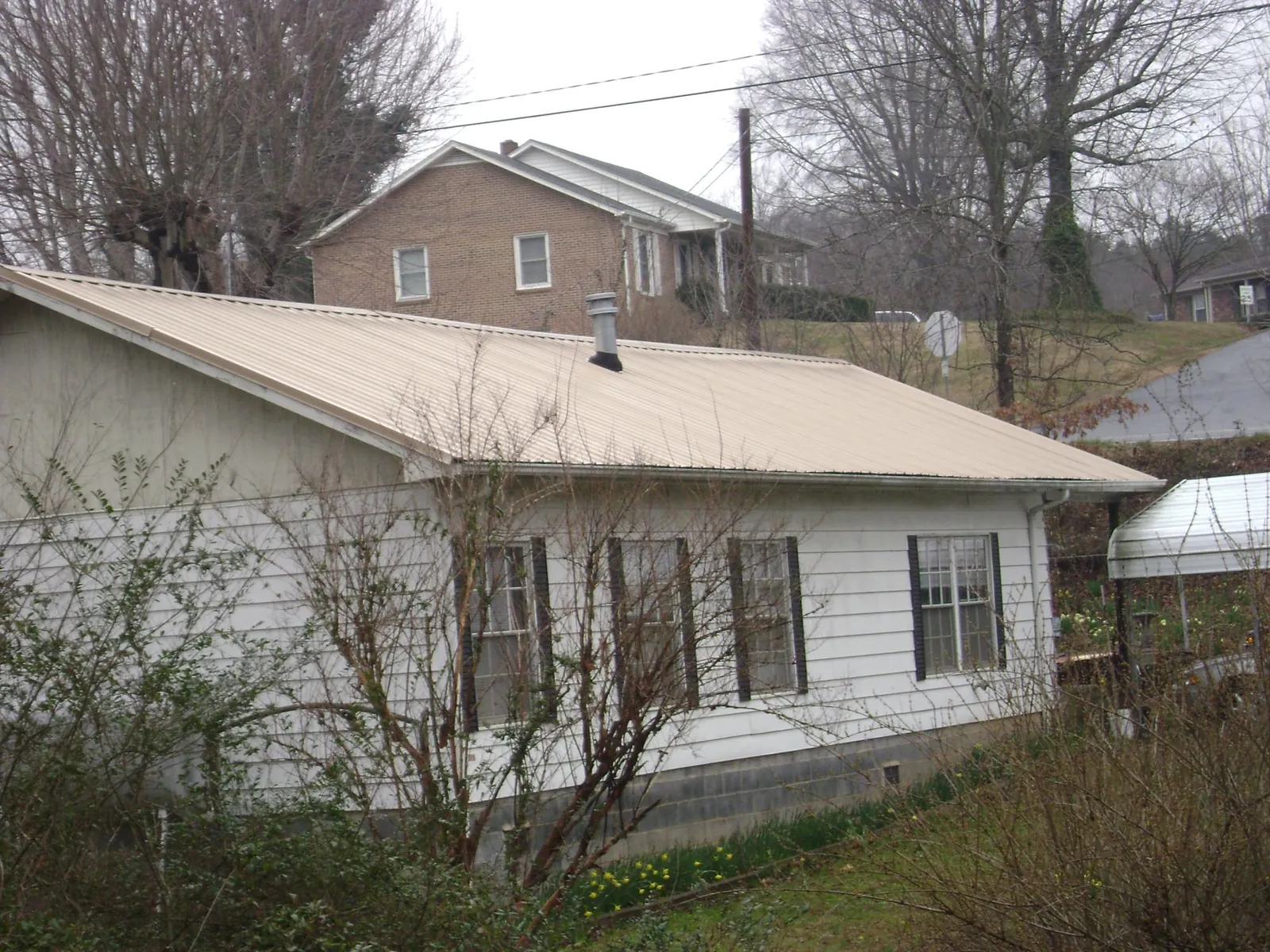 Tan metal roof on a white sided house set into a hillside — Commercial Roofing by Roofing Brothers in Kintnersville